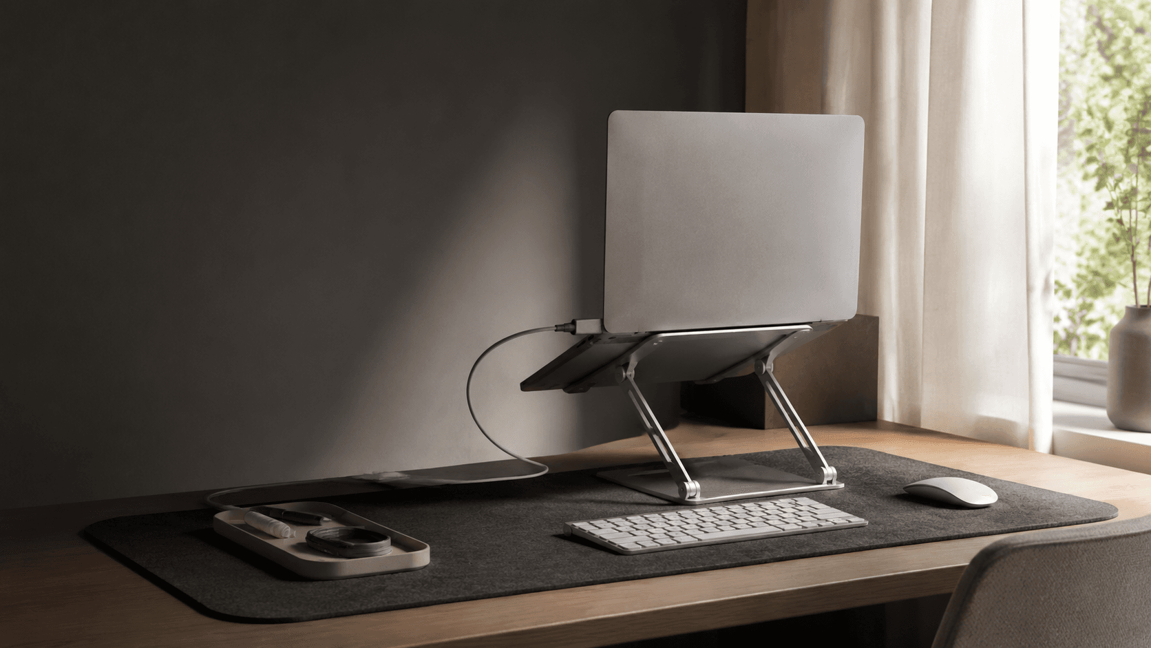 Organised home workspace with a folding laptop stand, desk mat and managed cables